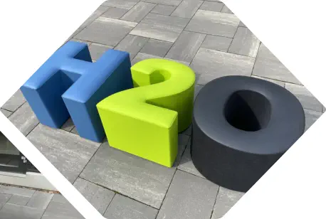 Sitzbuchstaben in Form von H2O in blau, grün und schwarz stehen auf Terasse