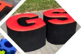 Buchstaben G und S als Hocker zum Sitzen stehen vor einer Wiese