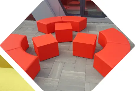 rote Würfelhocker und halbrunde Hocker Elemente stehen vor einem Büro